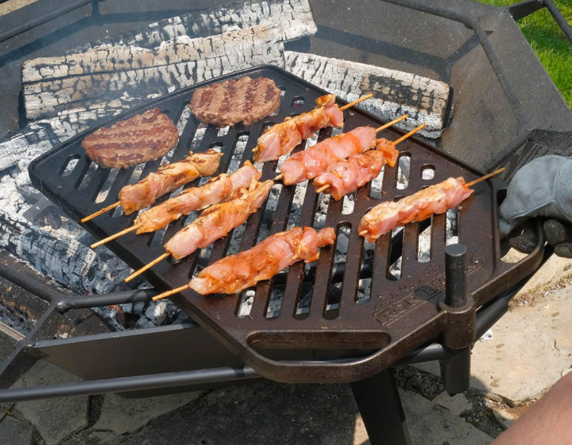 Plate BBQ grill with burgers and skewers over the fire
